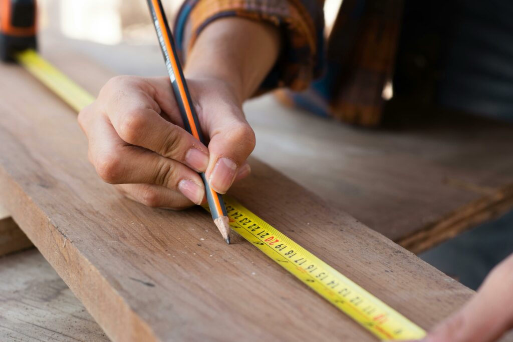 person using a tape measure and a pencil on a piece of wood