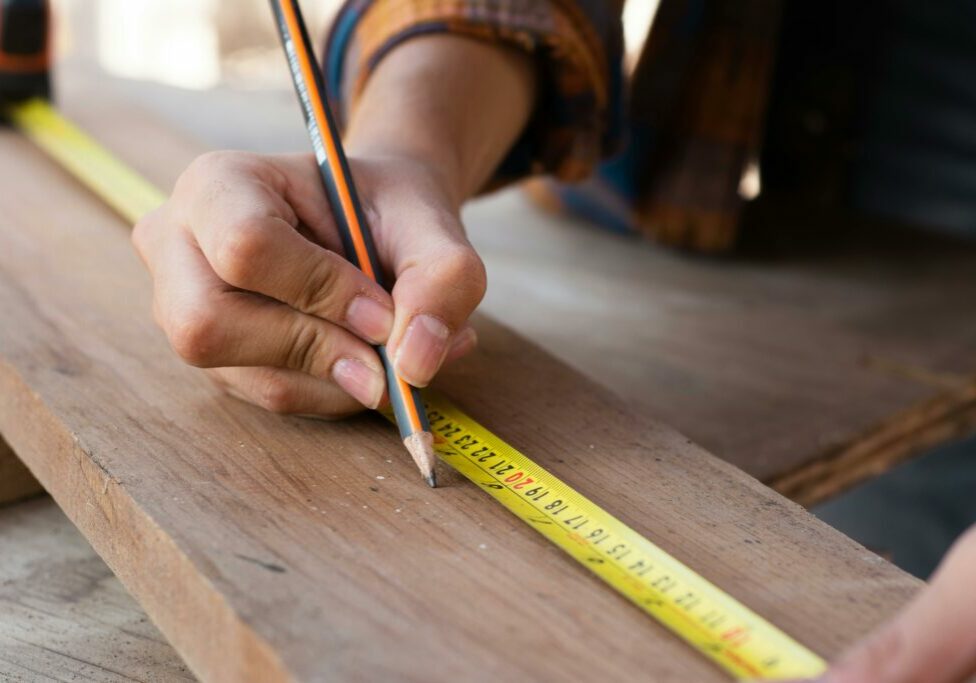 person using a tape measure and a pencil on a piece of wood
